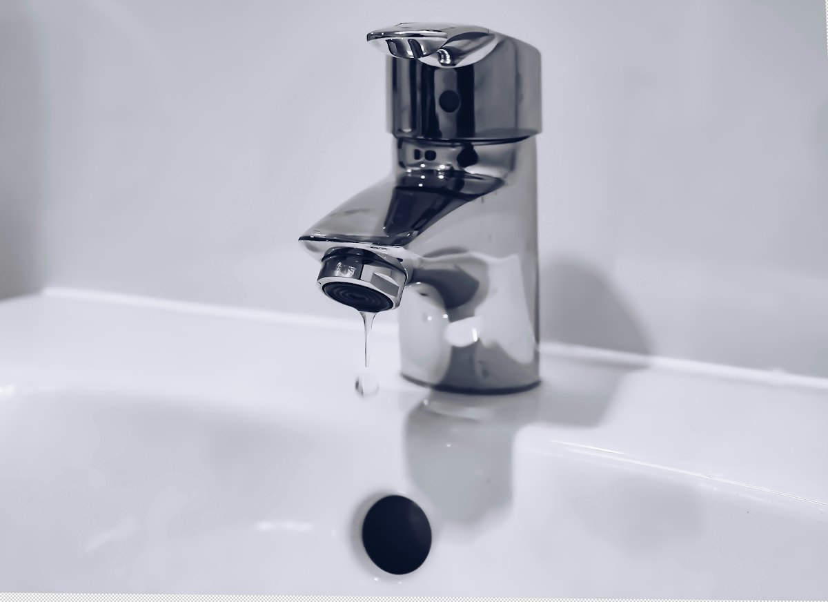 Stainless steel mixer tap running water into a white basin